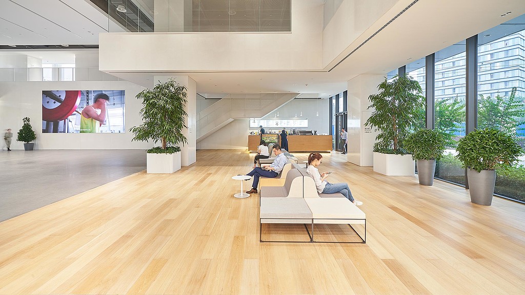 A couple of women sitting on a couch in a room with large windows.